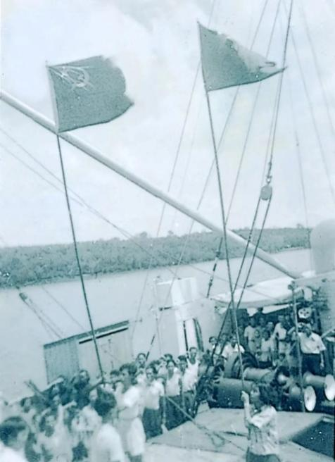 1953年在“大伟健轮”上，被遣送回国的难侨难掩兴奋挥舞红旗，陈毅明为右侧举旗者。.png